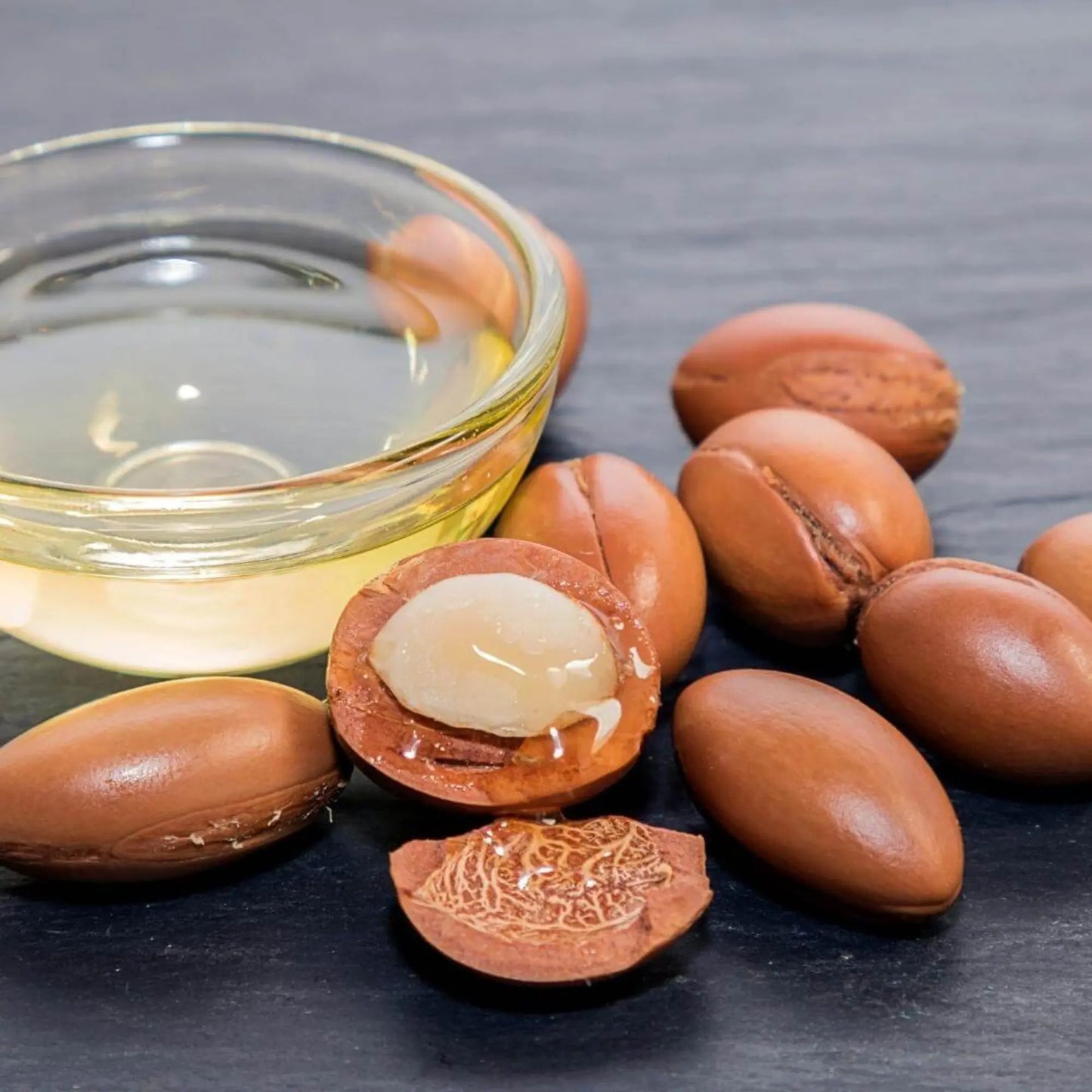 Glass bowl of pure argan oil from Morocco surrounded by argan nuts — a nourishing hair and skin treatment known as Moroccan argan oil, ideal for healing shine, frizz control, and deep skin hydration.