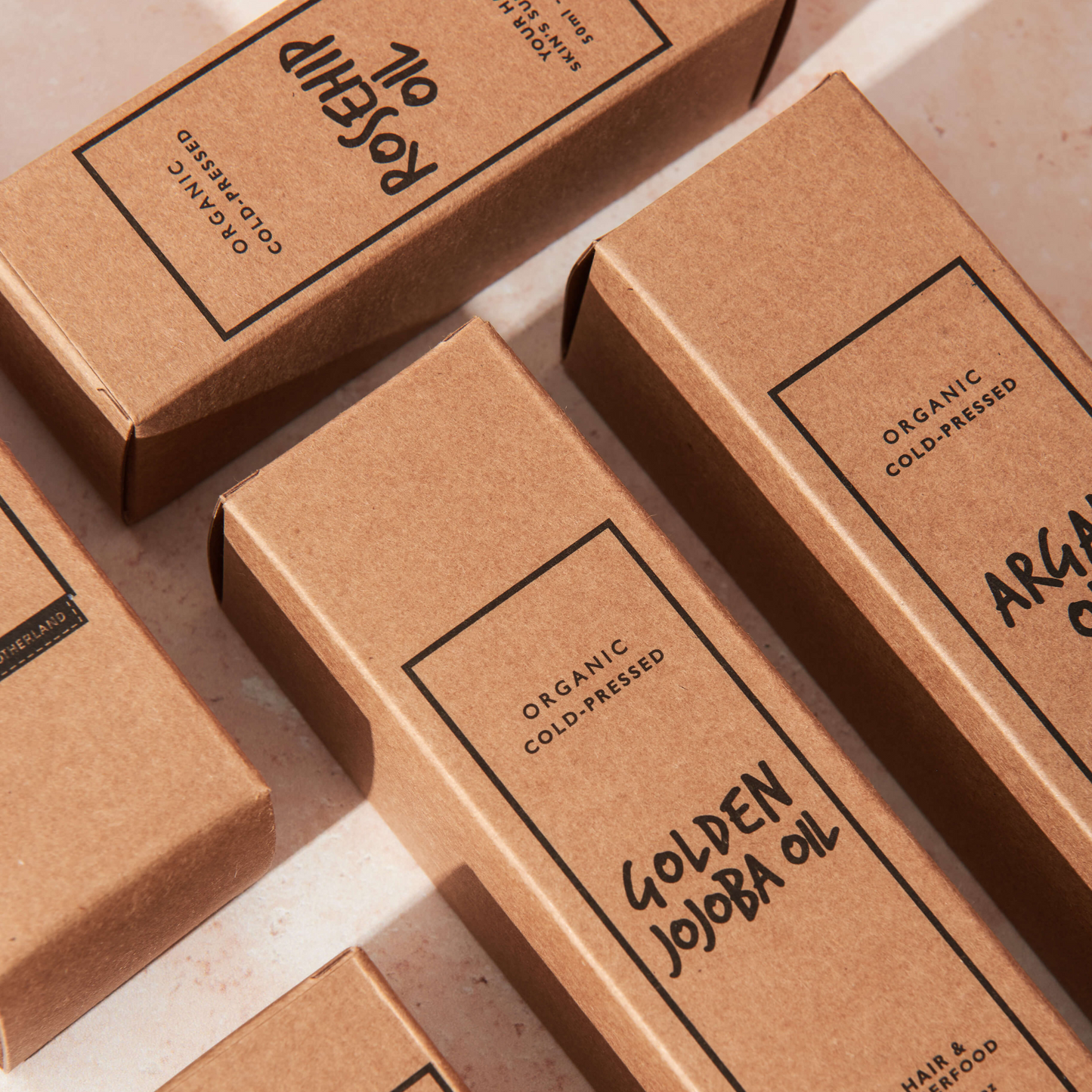 Flat lay of organic cold-pressed golden jojoba oil, rosehip oil, and argan oil in sustainable kraft packaging. Natural facial oils and hair oils for skin, nails, and scalp.