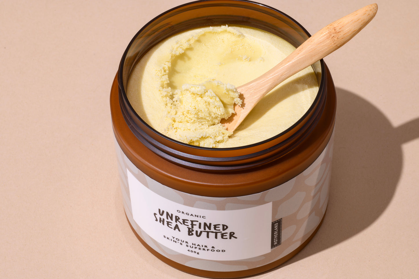 Jar of raw, unrefined organic shea butter with a wooden spoon, used as a natural moisturiser for skin, hair, lips, and body. Ideal for eczema and dry skin care.