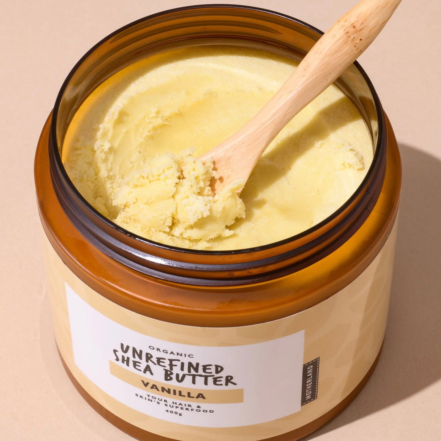 Scoop of organic vanilla-infused unrefined shea butter from a 400g Motherland Organics tub — perfect for moisturising dry skin, soothing eczema, and nourishing hair with natural African shea butter.
