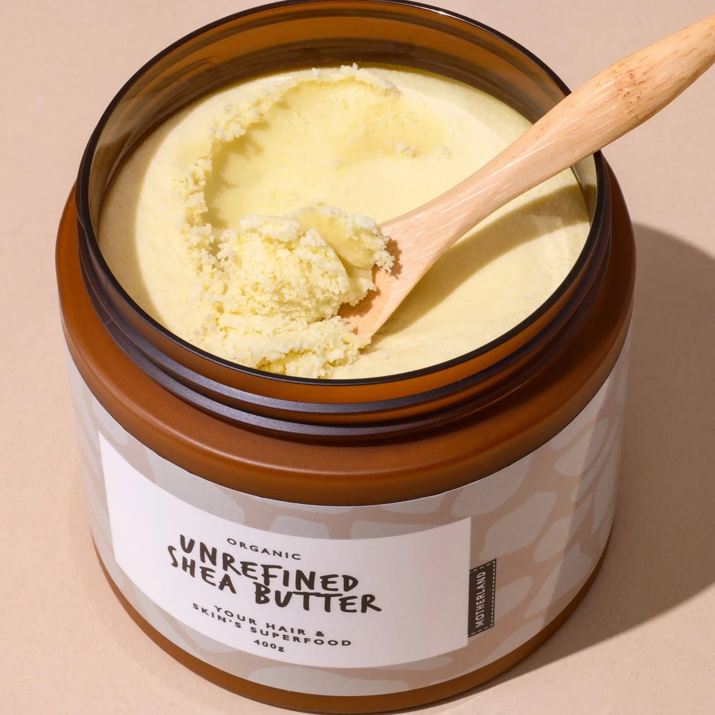 Spoon scooping raw unrefined shea butter from a 400g Motherland Organics tub — rich, natural skin and hair moisturiser ideal for dry skin, eczema relief, and daily body care using organic African shea butter.