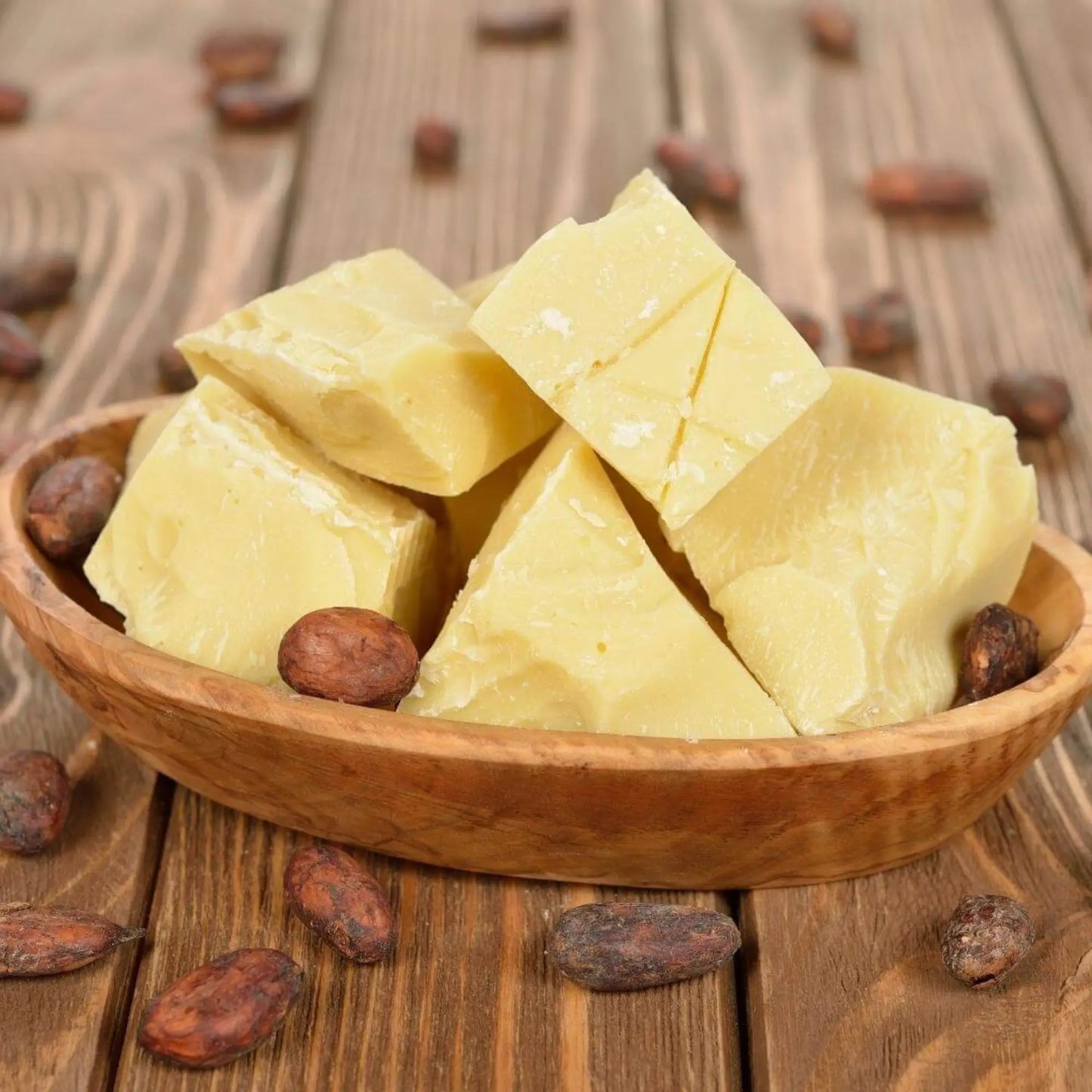 Chunks of raw organic cocoa butter in a wooden bowl surrounded by cocoa beans — ideal for use in cocoa butter face cream, moisturisers, hand creams, and cooking with raw cacao butter.