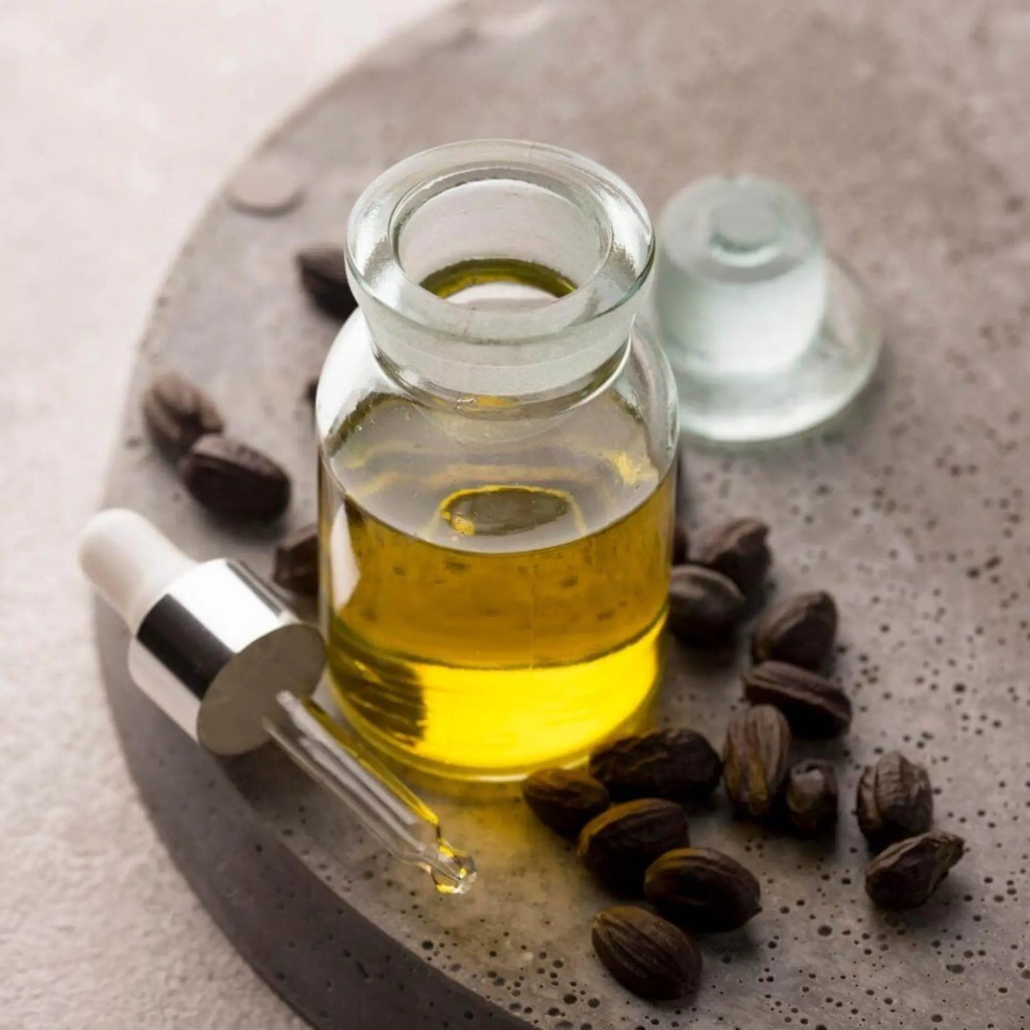 Glass bottle of organic jojoba oil with dropper, surrounded by jojoba seeds — lightweight, non-comedogenic oil ideal for face, hair, nails, and skin hydration.