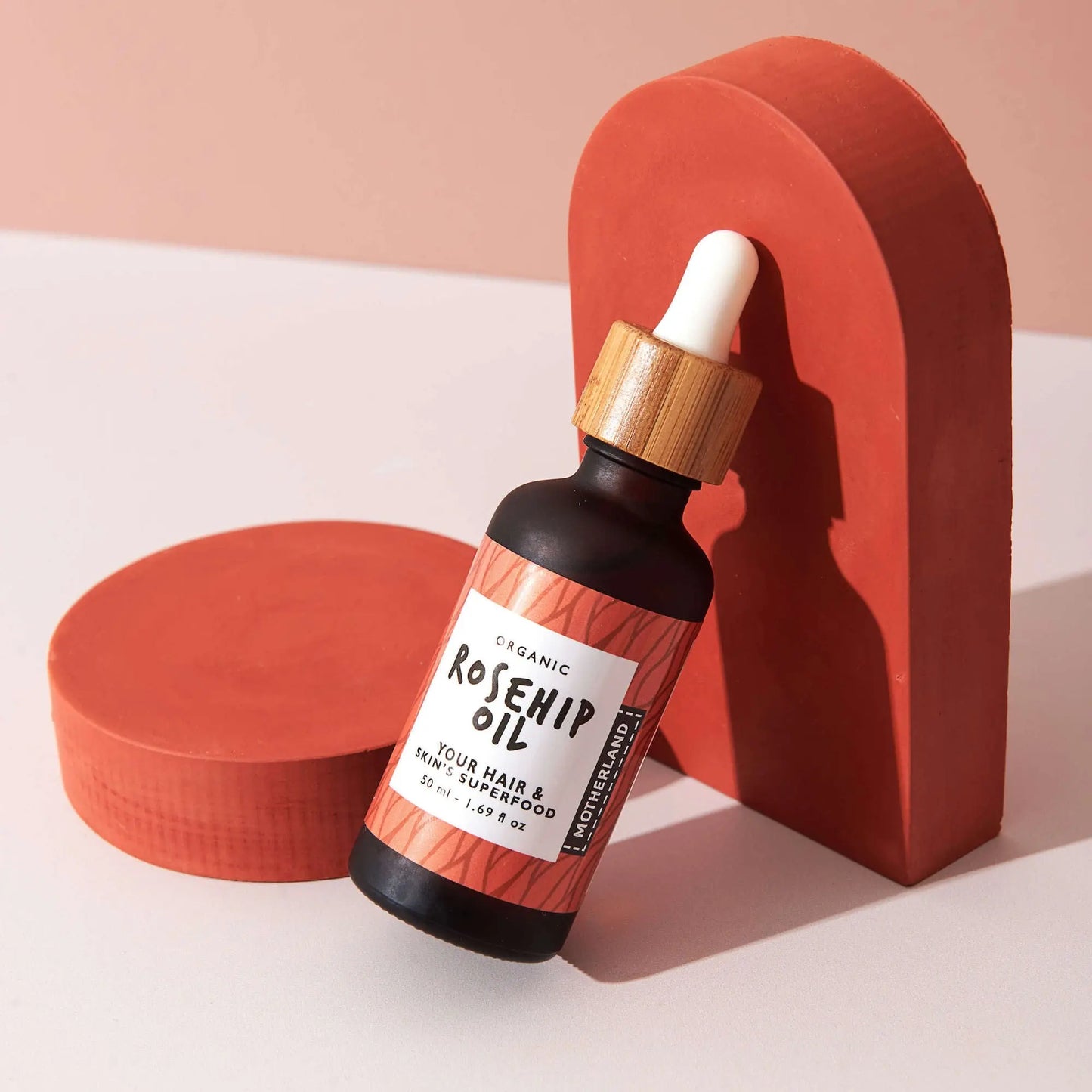 Organic rosehip oil bottle with bamboo dropper, rich in vitamins A and C for face, hair, and skin — ideal for scars, hyperpigmentation, and natural glow, styled on a modern terracotta-toned background.